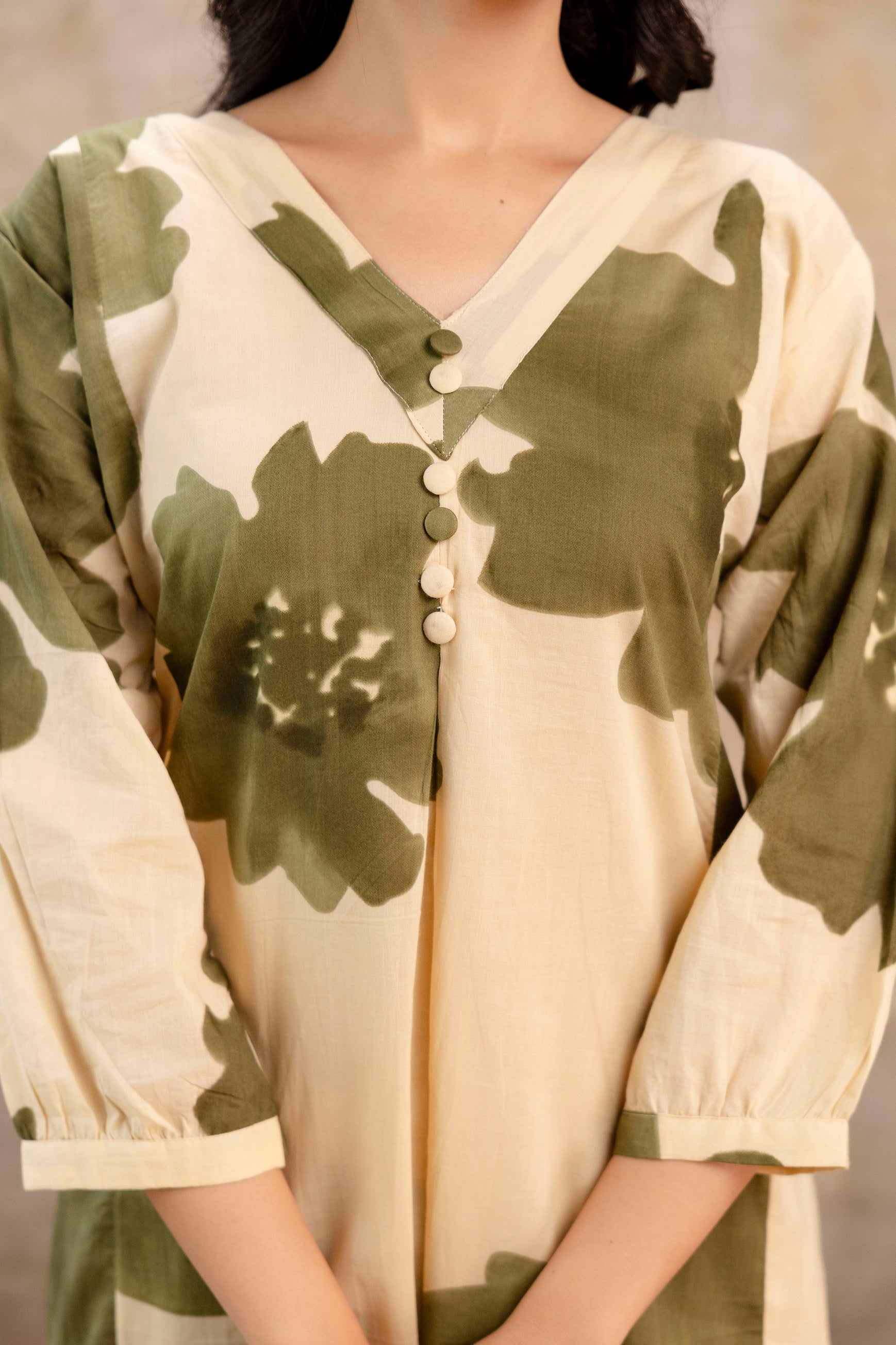 Close-up view of beige cotton kurti with large olive green floral prints

V-neckline featuring five round fabric-covered buttons

Soft pleating below neckline adds flow and detail

3/4th sleeves with light gathers and plain cuffs

Elegant handcrafted design suitable for ethnic and casual wear