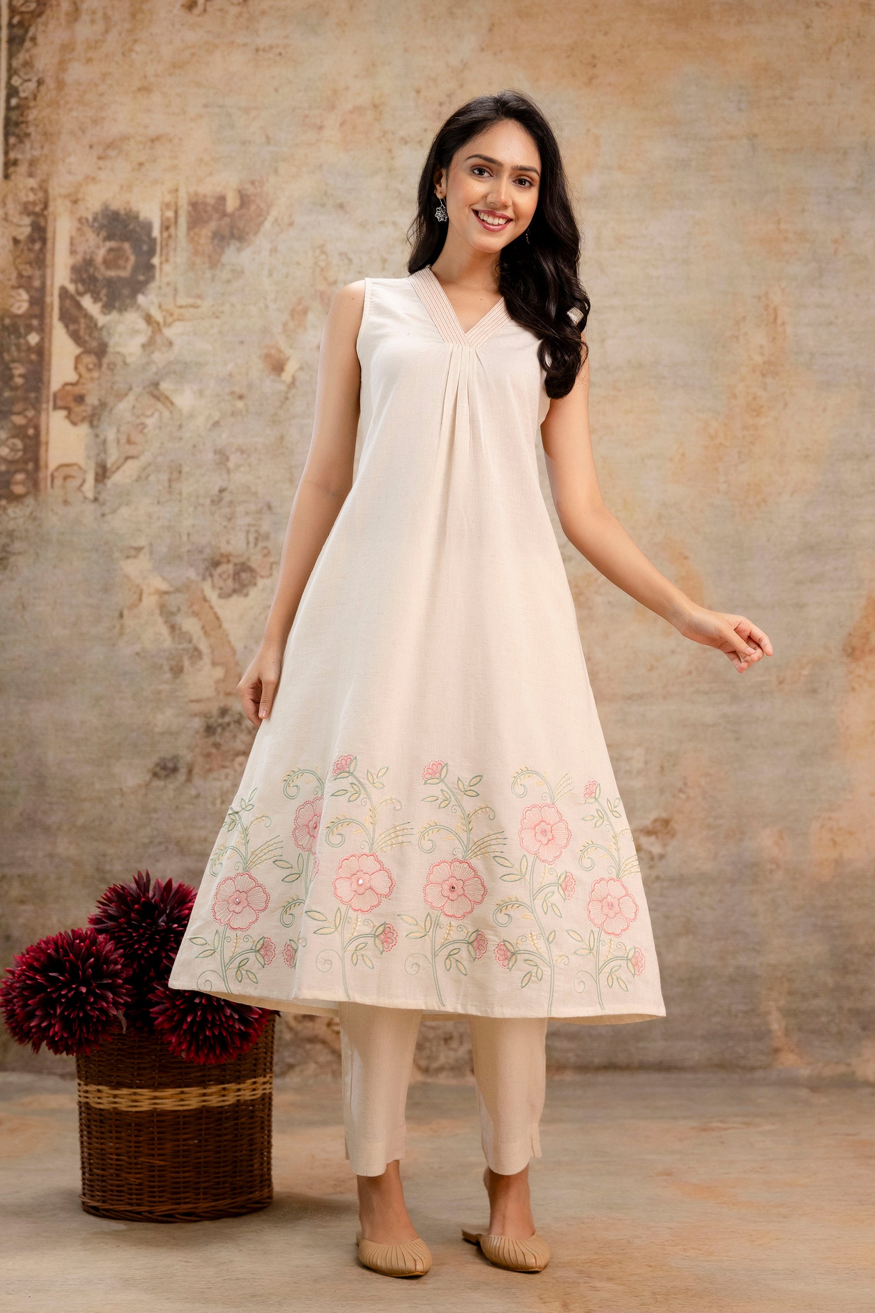 Sleeveless ivory Tanauri cotton kurti with soft flare and pleated neckline.

Features delicate floral embroidery in pink and green along the hemline.

Paired with neutral-tone straight pants for a complete ethnic look.

Lightweight and breathable, perfect for summer or casual occasions.

Styled with simple accessories and traditional footwear.

Keywords: floral cotton kurti, Tanauri kurti set, sleeveless ethnic wear, summer Indian outfit.