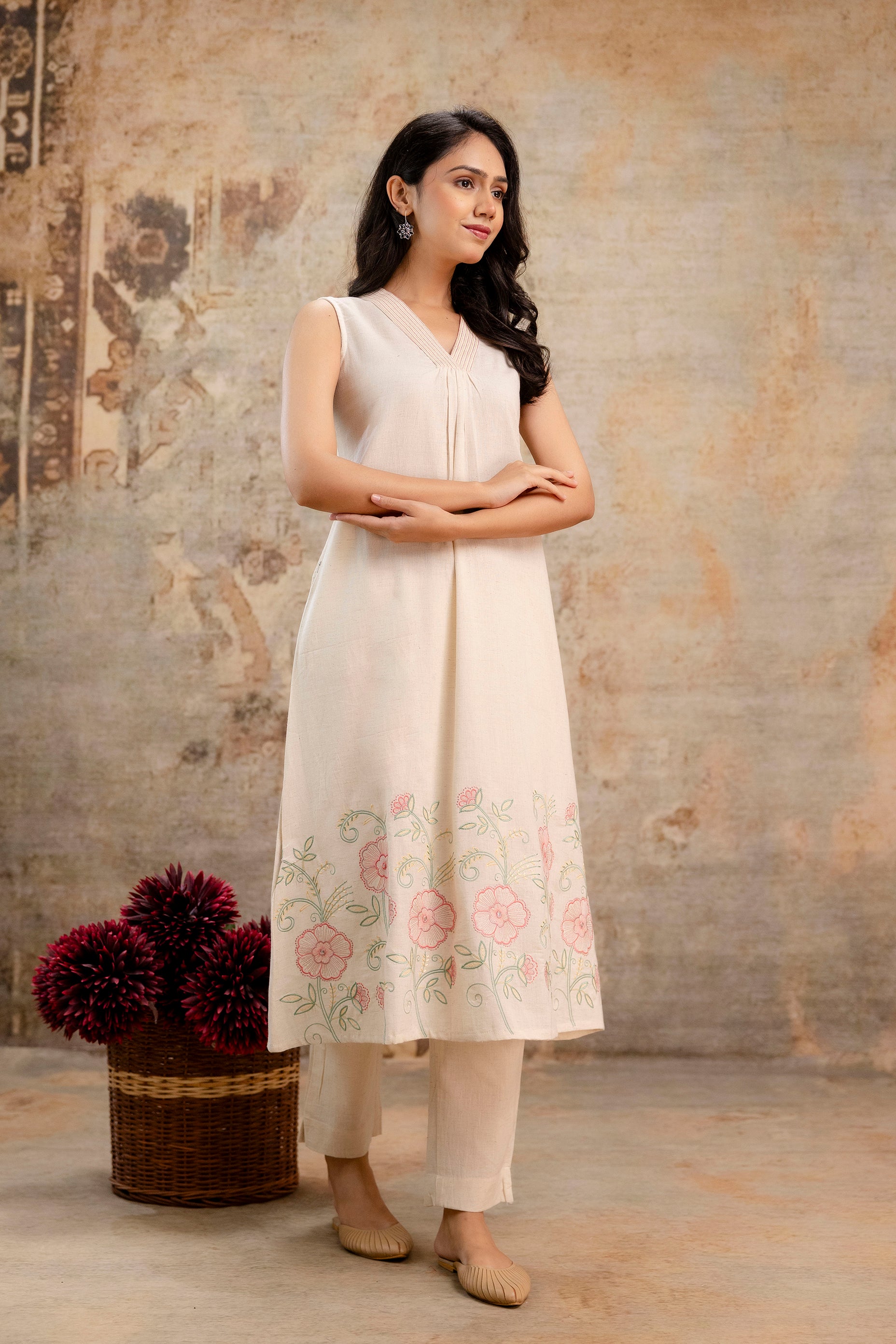 Graceful sleeveless ivory cotton kurti by Tanauri with V-neck pleat detailing.

Intricately embroidered floral border in shades of pink and green at the hemline.

Paired with solid ivory straight pants for a soft monochrome look.

Perfect for summer elegance, office ethnicwear, or light festive wear.

Keywords: Tanauri kurti set, embroidered cotton kurti, ivory sleeveless kurti, ethnic summer outfit.