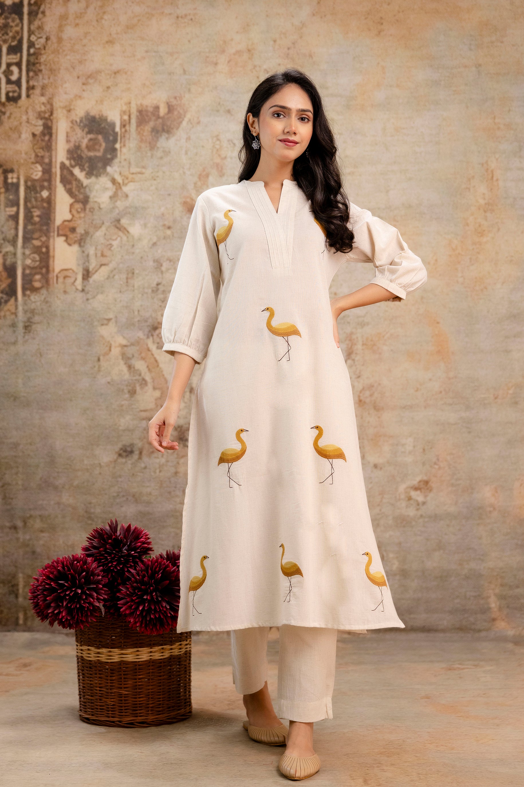 Elegant ivory A-line kurti with full sleeves from Tanauri.

Features hand-painted golden bird motifs across the front panel.

Mandarin collar with pleated detailing around the neckline for a sophisticated look.

Paired with matching ivory straight pants, creating a subtle yet graceful ensemble.

Made with soft, breathable cotton perfect for casual or festive daywear.

Keywords: bird motif kurti, Tanauri ivory ethnic wear, cotton kurti with sleeves, printed kurti for women, summer Indian outfit.
