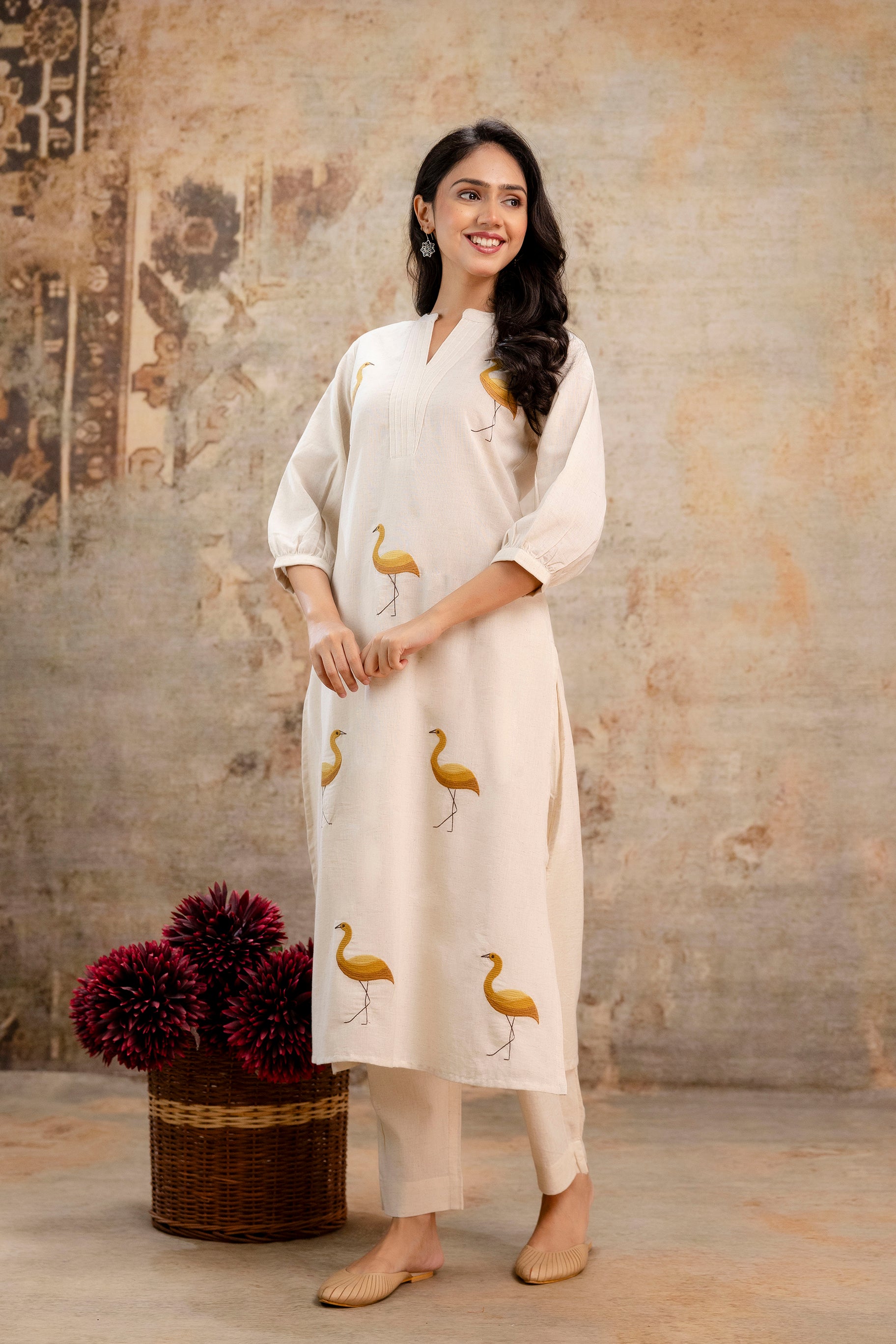 Graceful ivory kurti set featuring mustard yellow bird prints throughout the front.

Three-quarter balloon sleeves with soft gathers at cuffs add volume and charm.

Kurti includes a V-slit mandarin collar with fine pintuck detailing on the yoke.

Coordinated with matching ivory ankle-length pants for a complete look.

Crafted in lightweight cotton-blend fabric – ideal for all-day summer wear.

Keywords: bird printed kurti set, ivory ethnic co-ord, cotton kurti with pintucks, women’s summer kurta pant set, 