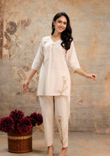 Full-length view of a woman wearing a cream-colored co-ord set.
Kurti features subtle brown floral embroidery on the top left and lower right.