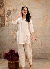 Smiling woman posing in an elegant cream co-ord set. Kurti with brown floral embroidery on the left chest and lower right hem.
