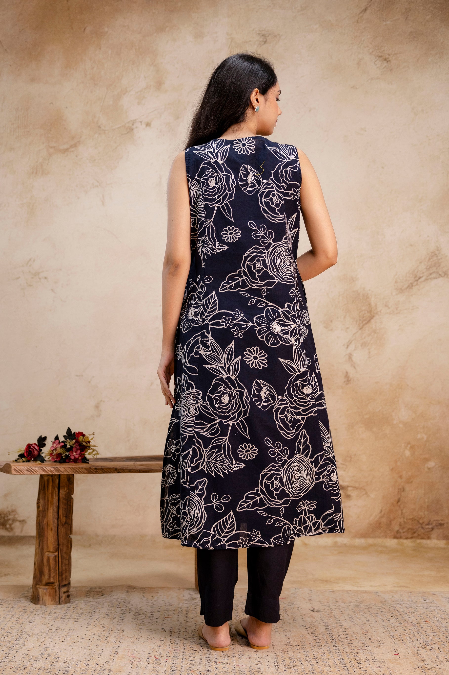 Back view of a navy blue sleeveless kurti featuring bold white floral print throughout.

A-line silhouette with a slightly flared hem for a graceful fall.

High-quality stitching and seamless finish visible from the back.

Paired with matching navy pants for a coordinated ethnic look.

Showcases the complete floral motif pattern continuing to the back.

Ideal visual for highlighting full 360-degree product design.