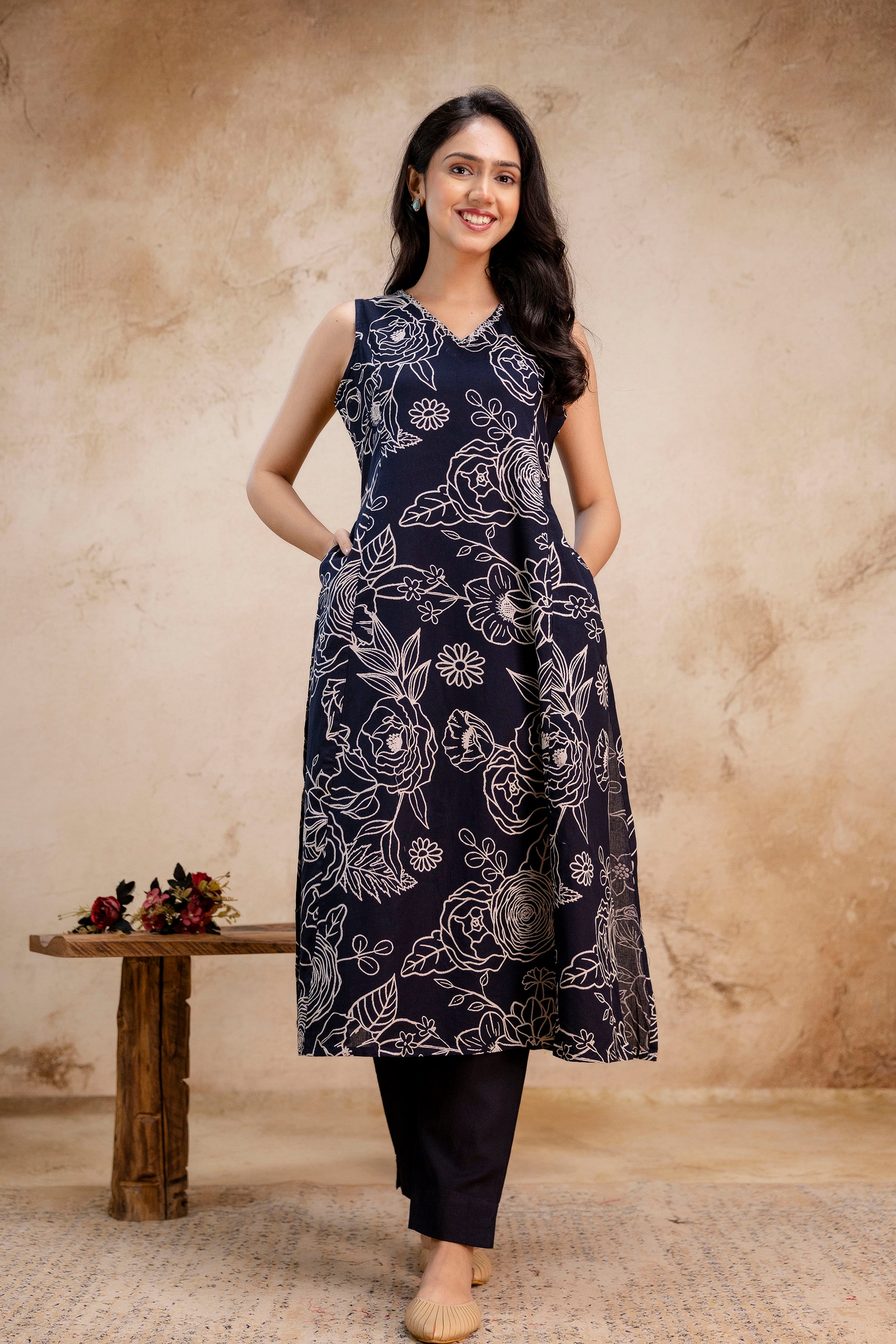 Model wearing a navy blue sleeveless kurti with white floral prints in a classic A-line cut.

Features side pockets for practical styling and added comfort.

Bold white botanical pattern stands out against the rich navy fabric.

Styled with matching navy cigarette pants for a monochromatic look.

Elegant V-neck design enhances the neckline and provides a modern silhouette.

Ideal for summer outings, casual gatherings, or festive daytime wear.