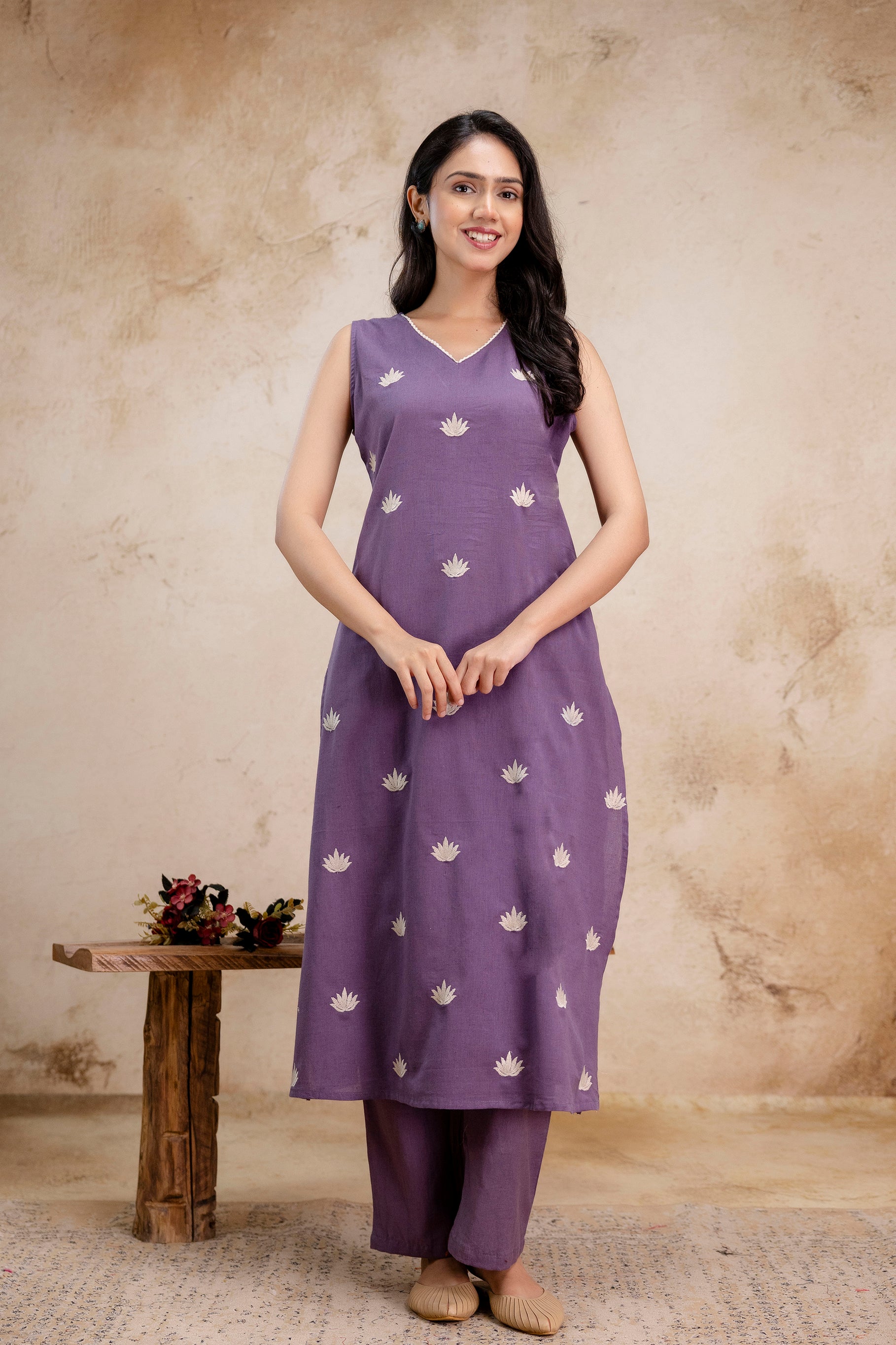 Sleeveless lavender kurti with a subtle V-neckline

Decorated with small, white lotus-shaped embroidered motifs throughout

Features gentle pleating under the neckline for added fall and structure

A-line silhouette that flares slightly below the waist

Made from a soft, breathable fabric with a smooth, elegant finish

Minimalist and graceful design ideal for casual or semi-formal wear
