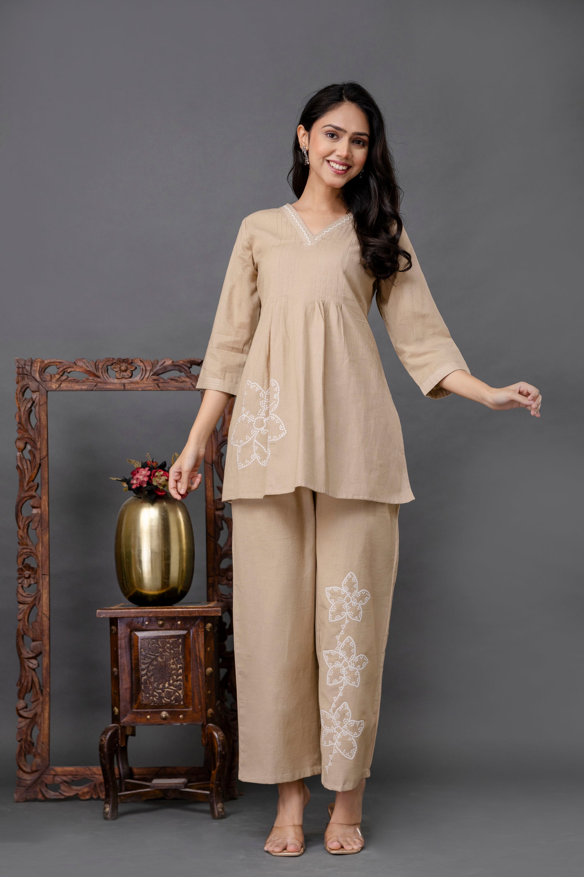 Beige cotton coord set featuring a short kurti and matching pants.

Kurti has a soft flare from under the bust, offering a relaxed silhouette.

V-neckline of the kurti is accented with delicate white embroidery.

3/4th sleeves in a straight cut, matching the minimal aesthetic.

Kurti’s left hem features a large, white floral embroidered motif.

Matching straight-fit pants with three embroidered white flowers on one leg.

Entire coord set is in the same beige tone, creating a seamless and elegant look.