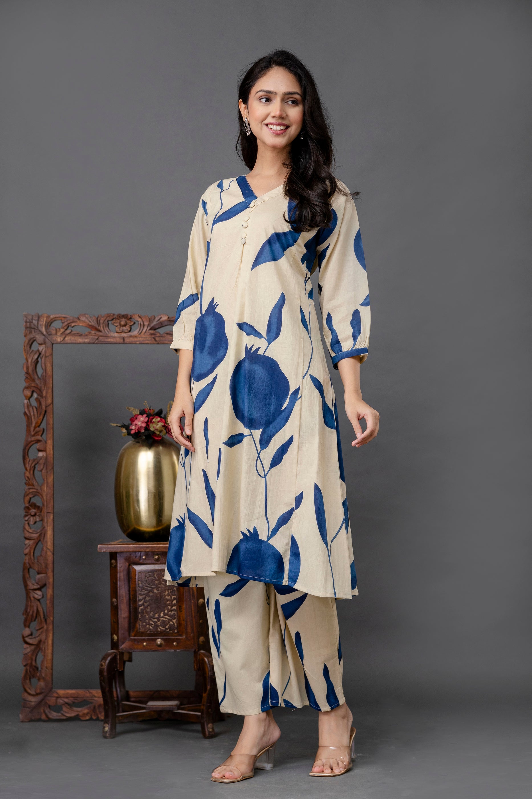 Beige kurta with bold navy blue pomegranate-style floral print

Straight-cut silhouette with soft gathers below neckline

Features round neckline with small central buttons

Three-quarter sleeves with matching print

Coordinated printed pants and nude heels for a minimal look

Model poses against a plain grey backdrop for contrast