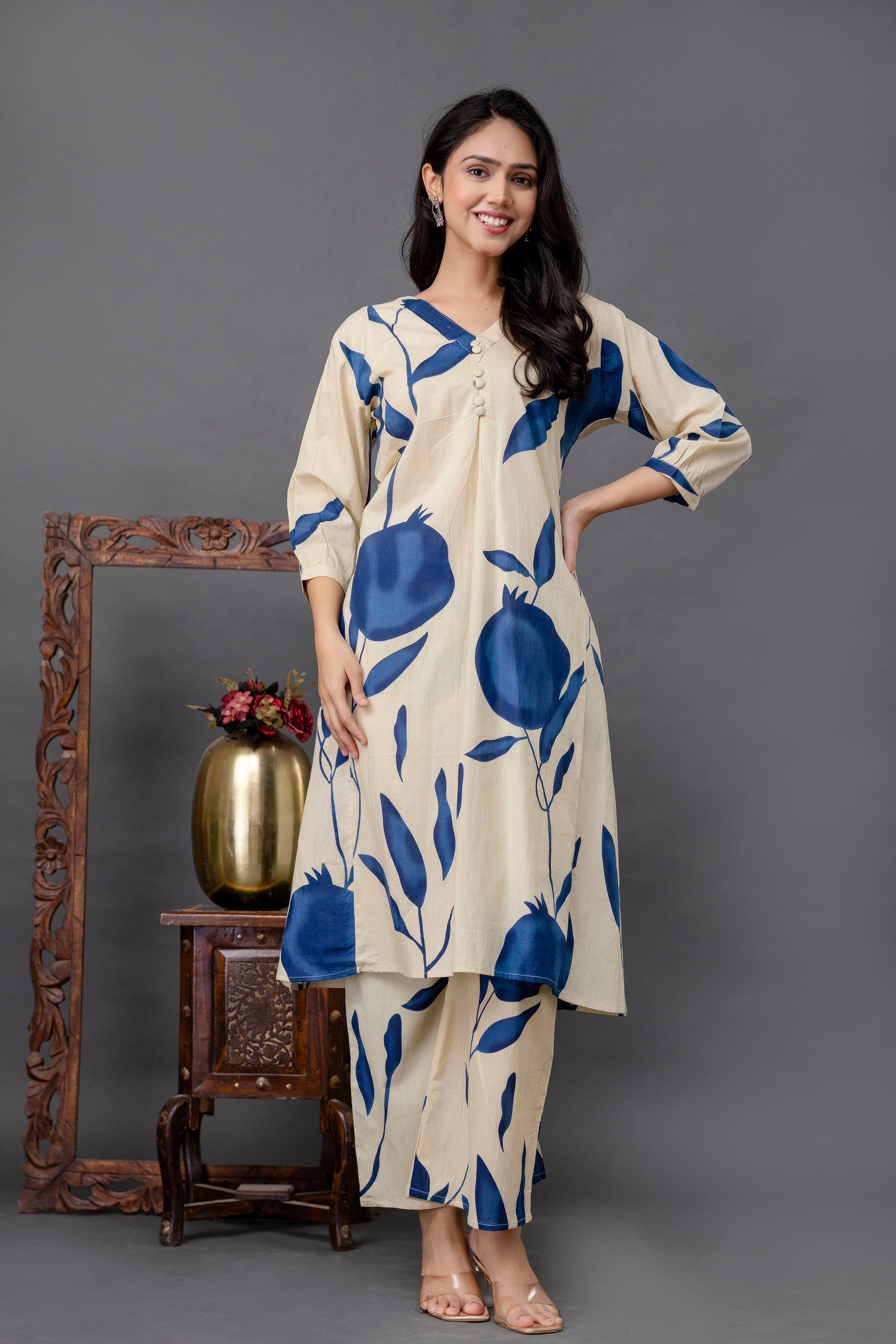 Beige A-line kurta featuring oversized navy pomegranate prints

Front button detail below the round neckline

Three-quarter sleeves with matching bold prints

Paired with coordinated beige trousers with the same blue design

Model standing against a plain grey backdrop with one hand on waist

Nude heels complete the clean, contemporary look