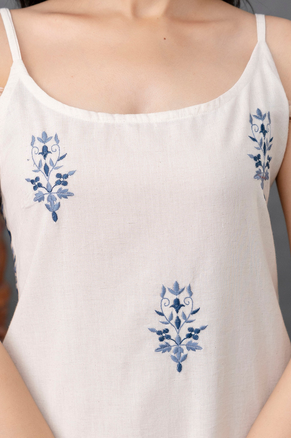 Detailed view of ivory sleeveless kurti in breathable cotton

Fine navy blue floral embroidery on chest and bodice

Features scoop neckline with thin shoulder straps

Minimalist summer ethnic wear with elegant handwork

Close-up emphasizes the soft texture and precise thread detailing