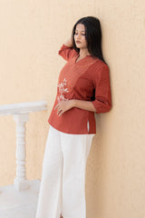 Woman wearing a red top and white pants against a beige wall.