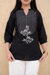 Person wearing a black kurta with white floral embroidery on a beige background
