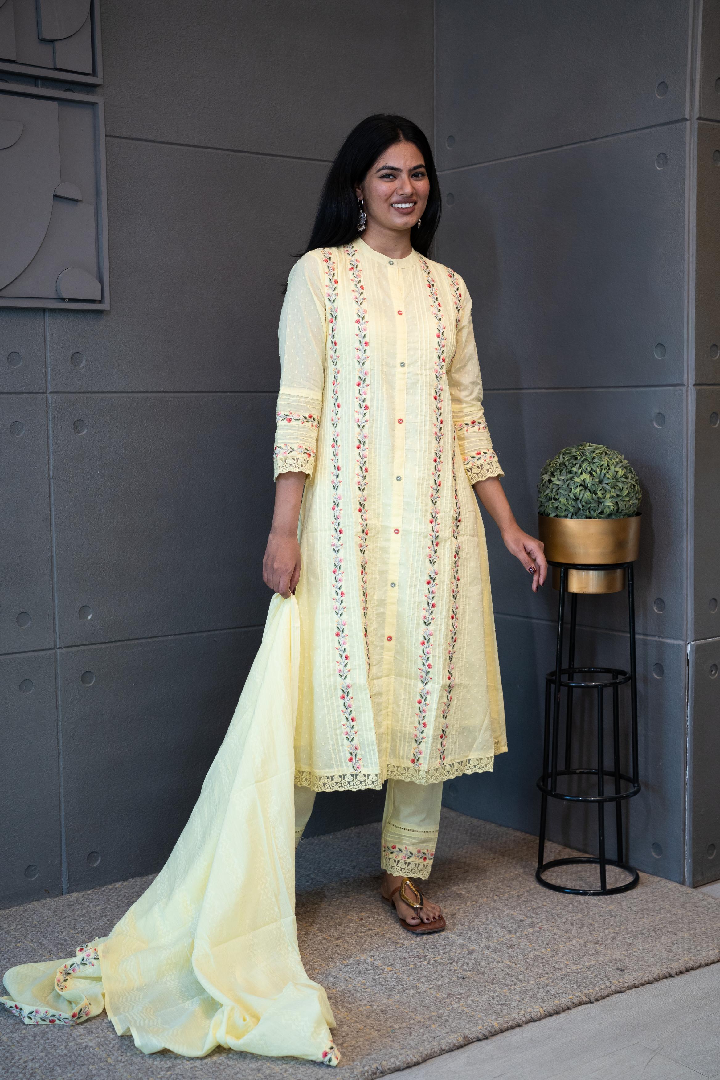 A woman modeling 'Sun Dew Dupatta Set' by Tanauri, featuring a light yellow cotton kurti and trousers with delicate multicolor embroidery, holding a textured, light yellow dupatta