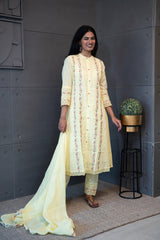 A woman modeling 'Sun Dew Dupatta Set' by Tanauri, featuring a light yellow cotton kurti and trousers with delicate multicolor embroidery, holding a textured, light yellow dupatta