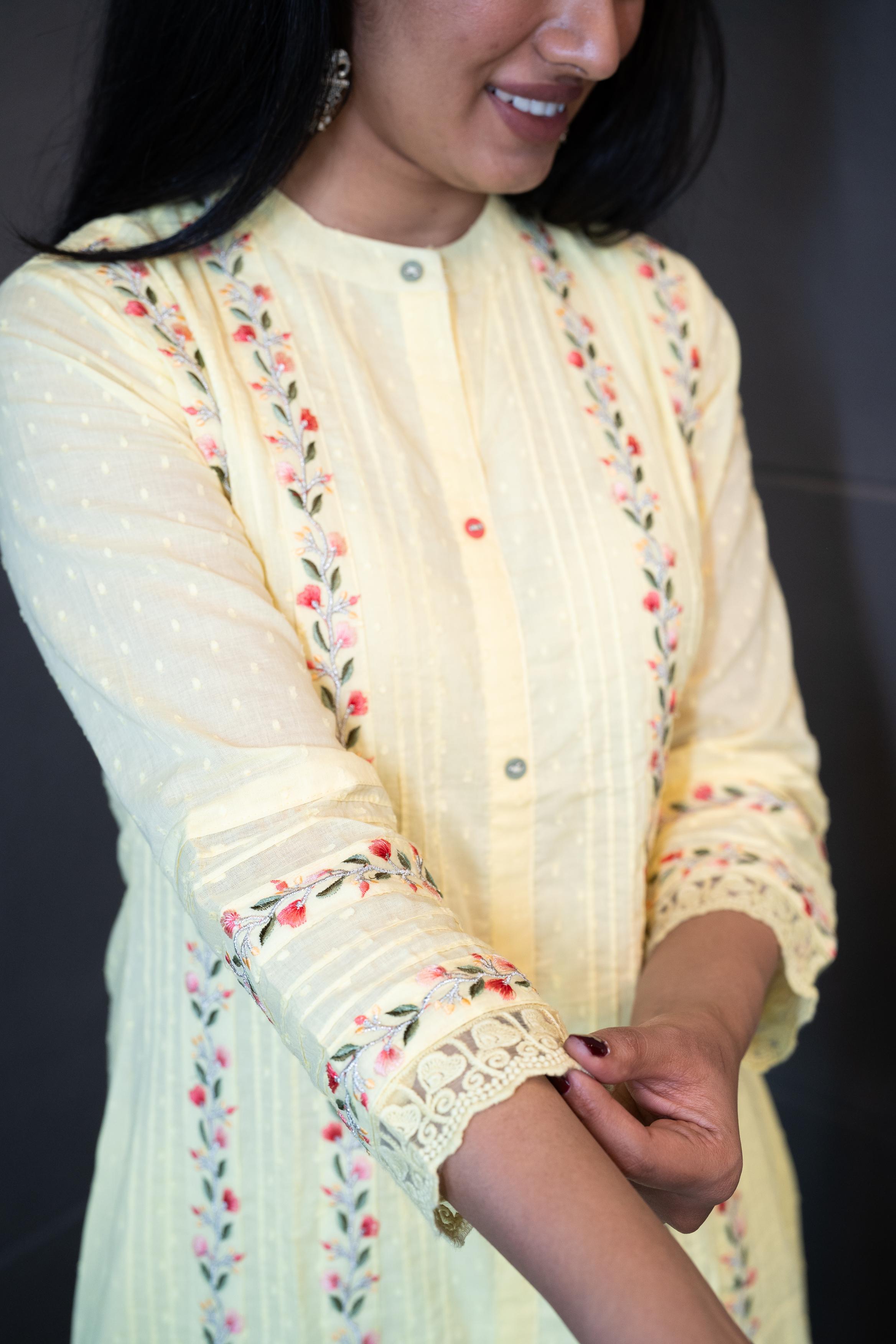A woman modeling 'The Sun Dew Dupatta Set' by Tanauri, featuring a light yellow cotton kurti and trousers with delicate multicolor embroidery, holding a textured, light yellow dupatta