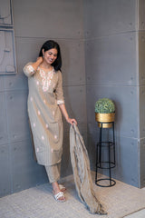 A woman wearing 'The Dusky Dupatta Set' by Tanauri, a long, light brown/khaki cotton kurti and matching trousers with delicate pink and white floral embroidery on the neckline, and holding a textured, dusty brown dupatta.