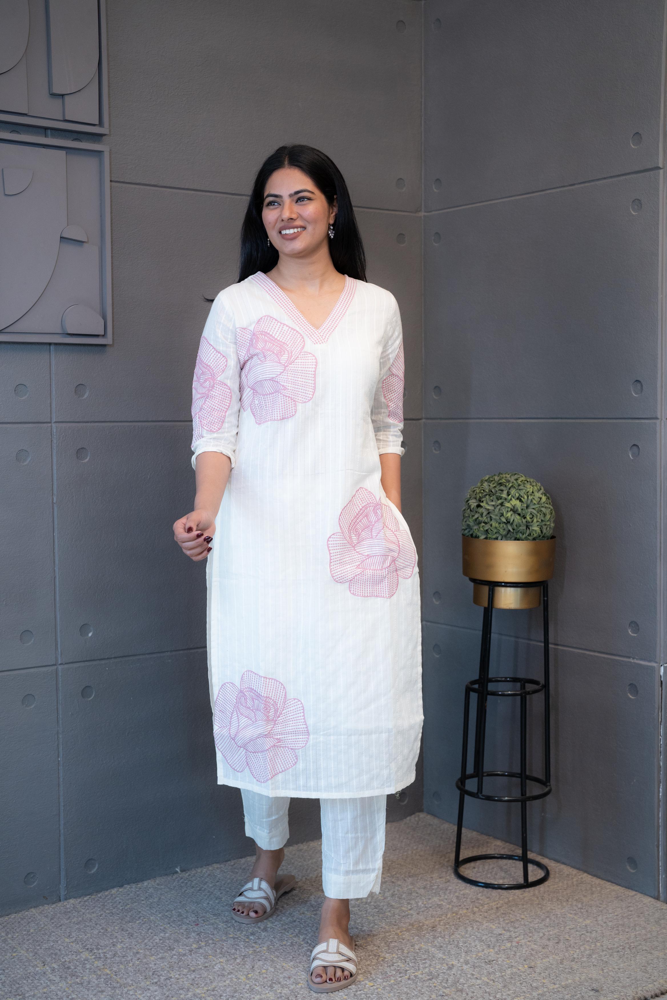 A woman modeling 'Pink Thread Kurta Set' by Tanauri, featuring a white cotton kurti and trousers with delicate pink floral embroidery