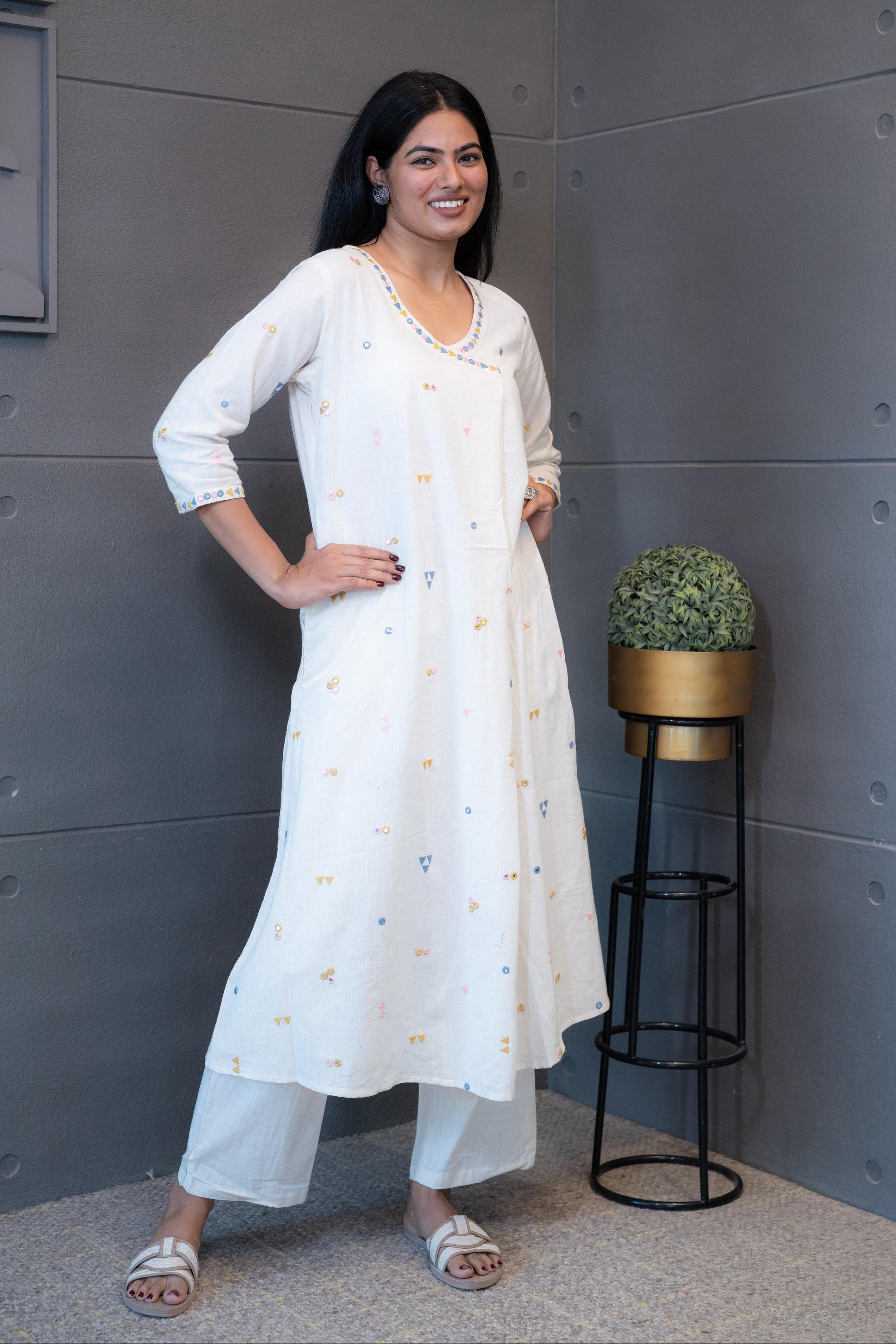 Close-up of the vibrant blue, pink, and yellow geometric triangle and circle embroidery on the cream cotton fabric of the Tanauri Kurta