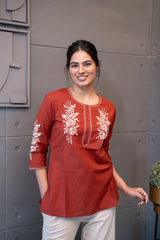 Model wearing Tanauri Sun Baked Rose Short Kurti/Top, displaying the terracotta cotton short kurti with white floral embroidery, paired with white pants for a fresh and elegant ethnic look