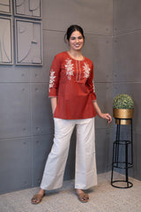 Model wearing Tanauri Sun Baked Rose Short Kurti/Top, displaying the terracotta cotton short kurti/top with white floral embroidery, paired with white pants for a fresh and elegant ethnic look