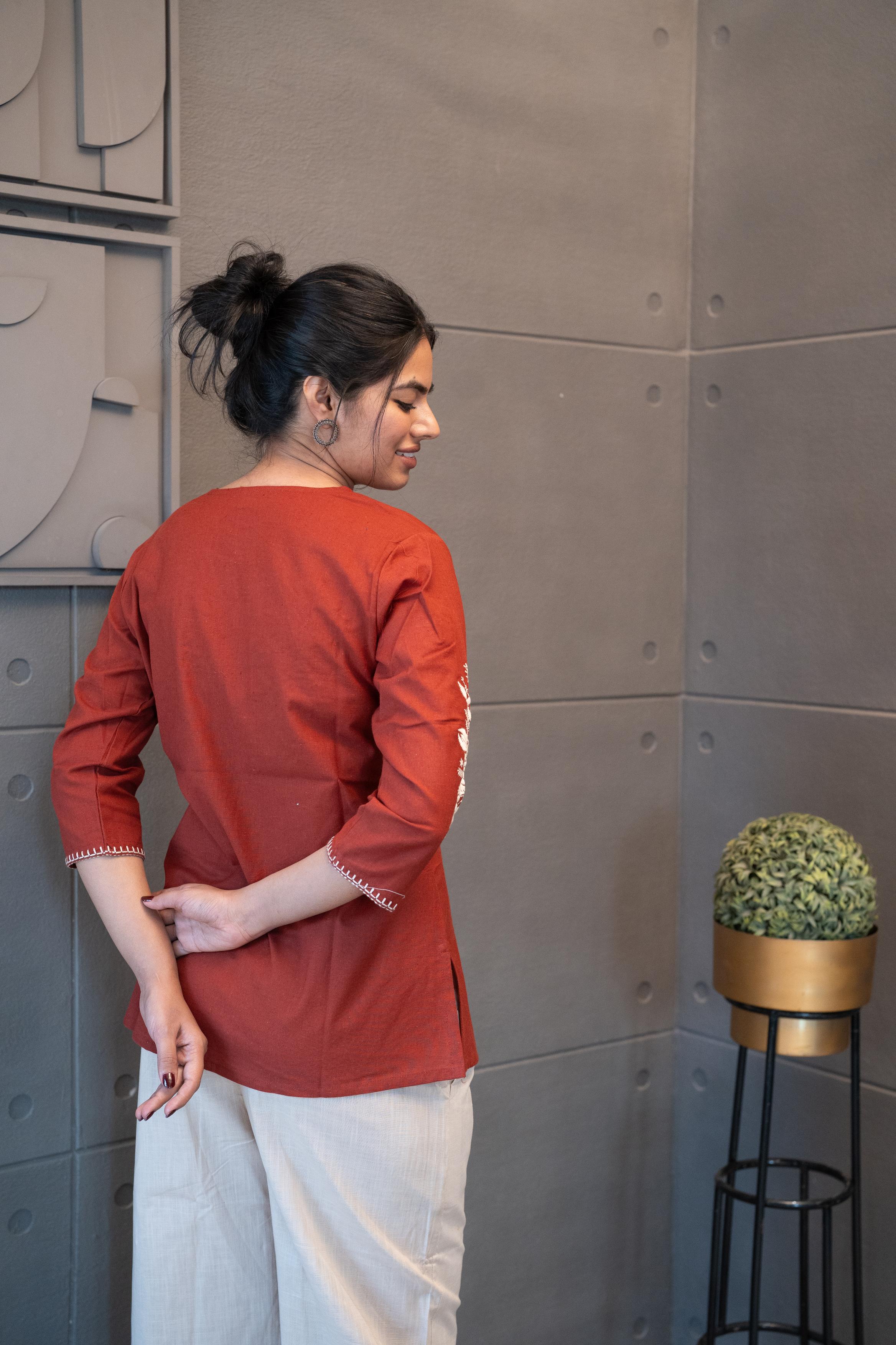 Tanauri Sun Baked Rose Short Kurti/Top, folded in clear packaging, showcasing a terracotta cotton tunic with prominent white floral rose and leaf embroidery on the front