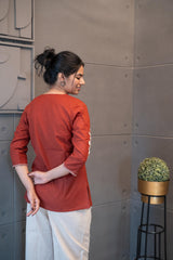 Tanauri Sun Baked Rose Short Kurti/Top, folded in clear packaging, showcasing a terracotta cotton tunic with prominent white floral rose and leaf embroidery on the front