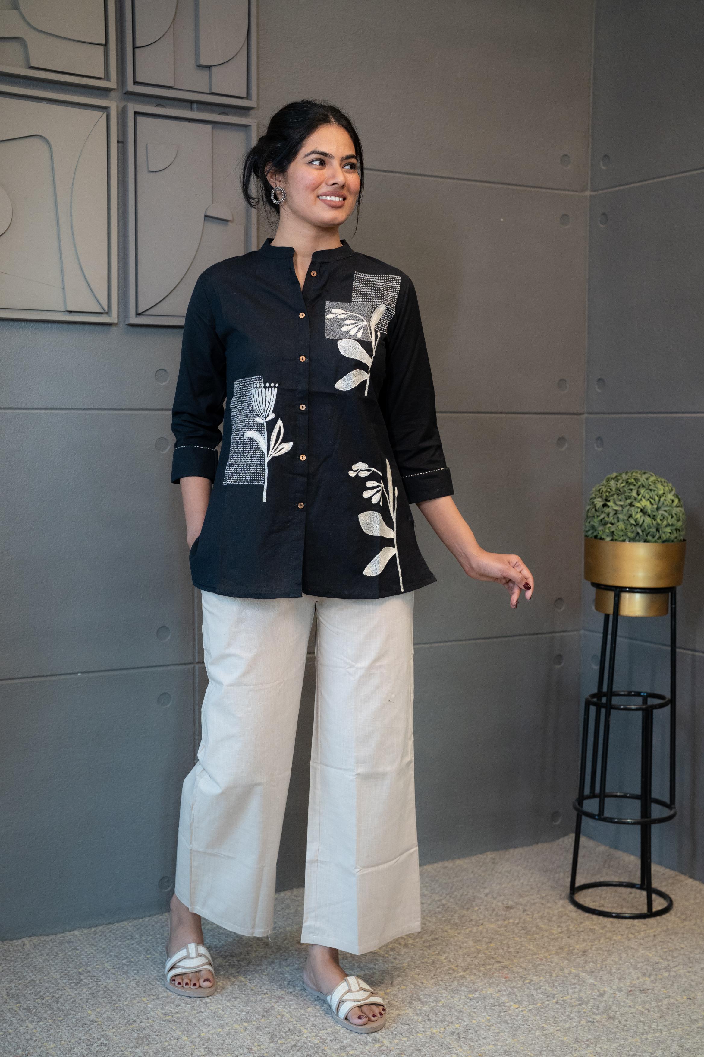 Model wearing Tanauri Black Floral Short Kurti/Top, displaying the black cotton short kurti with white floral and geometric designs, paired with white pants for a stylish ethnic-casual look