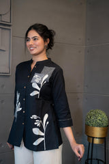 Model wearing Tanauri Black Floral Short Kurti/Top, displaying the black cotton short kurti/top with white floral and geometric designs, paired with white pants for a stylish ethnic-casual look