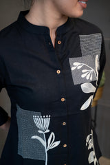 Close-up of the white floral and geometric embroidery/patchwork on the black fabric of the Tanauri Black Floral Short Kurti/Top, highlighting the intricate patterns