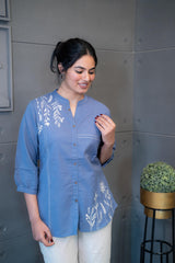 Model wearing Tanauri Blue Pop Short Kurti/Top, displaying the blue cotton short kurti with white leafy embroidery and band collar, paired with white pants for a fresh and elegant ethnic-casual look