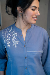 Tanauri Blue Pop Short Kurti/Top, folded in clear packaging, showcasing a blue cotton tunic with prominent white leafy embroidery on one side and a band collar with buttons