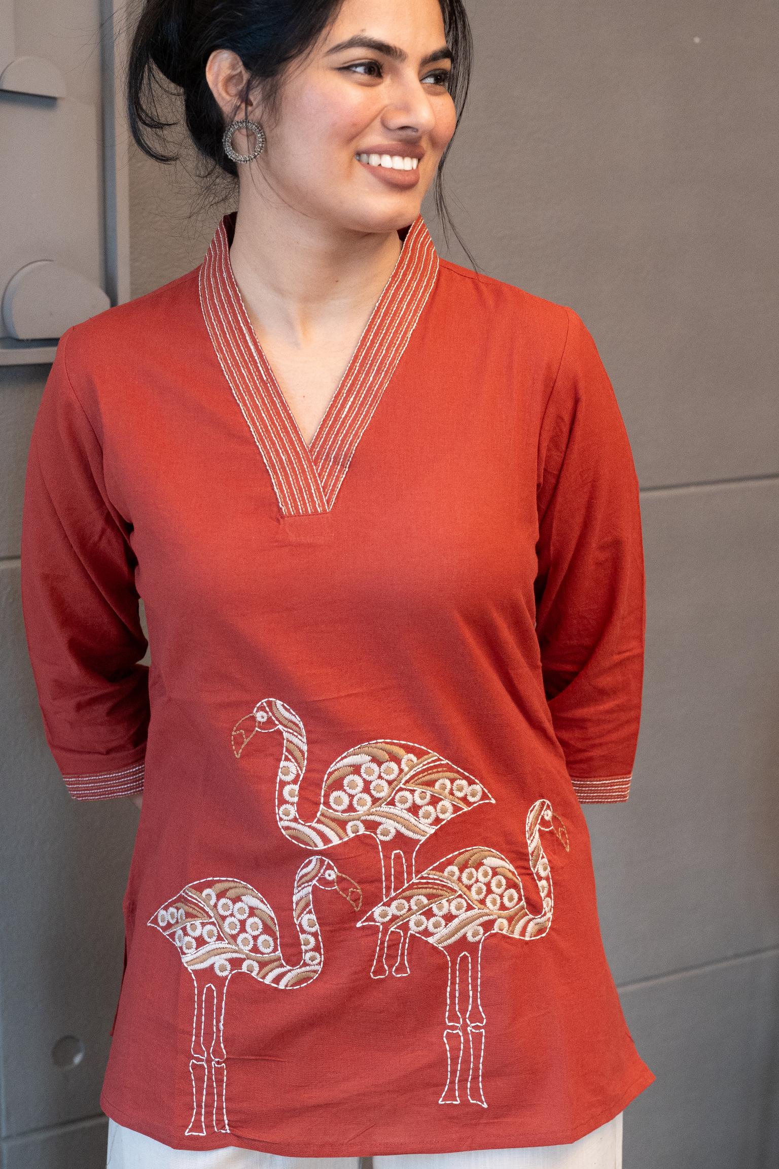 Model wearing Tanauri Mastani Short Kurti/Top, displaying the brick red cotton short kurti with V-neck stripe detail paired with white trousers, creating a chic ethnic-casual look