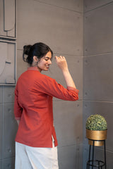 Model wearing Tanauri Mastani Short Kurti/Top, displaying the brick red cotton short kurti/top with V-neck stripe detail paired with white trousers, creating a chic ethnic-casual look