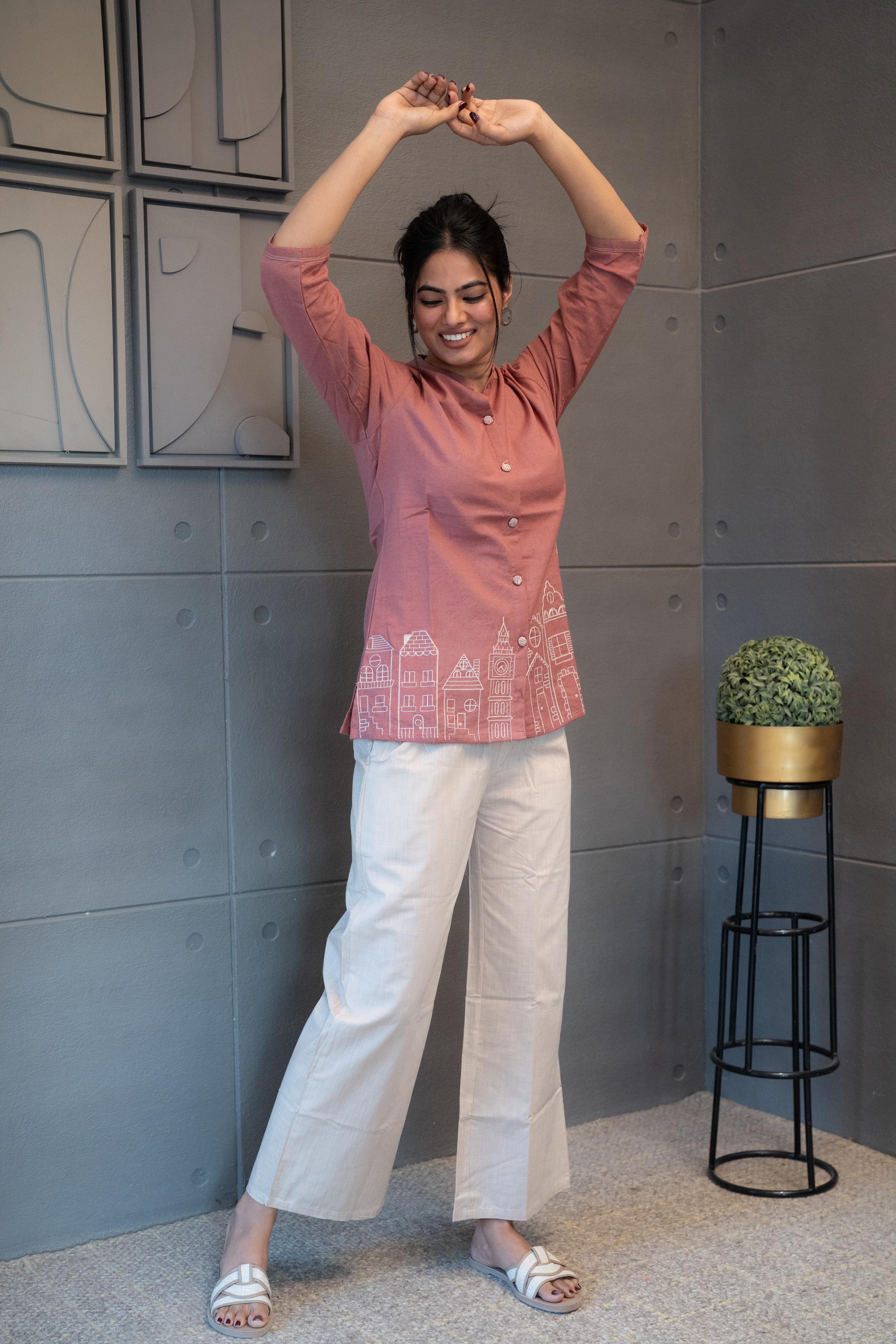Model wearing Tanauri Pink Cityscape Short Kurti/Top, displaying the blush pink cotton short kurti/top paired with white pants for a fresh and casual everyday look