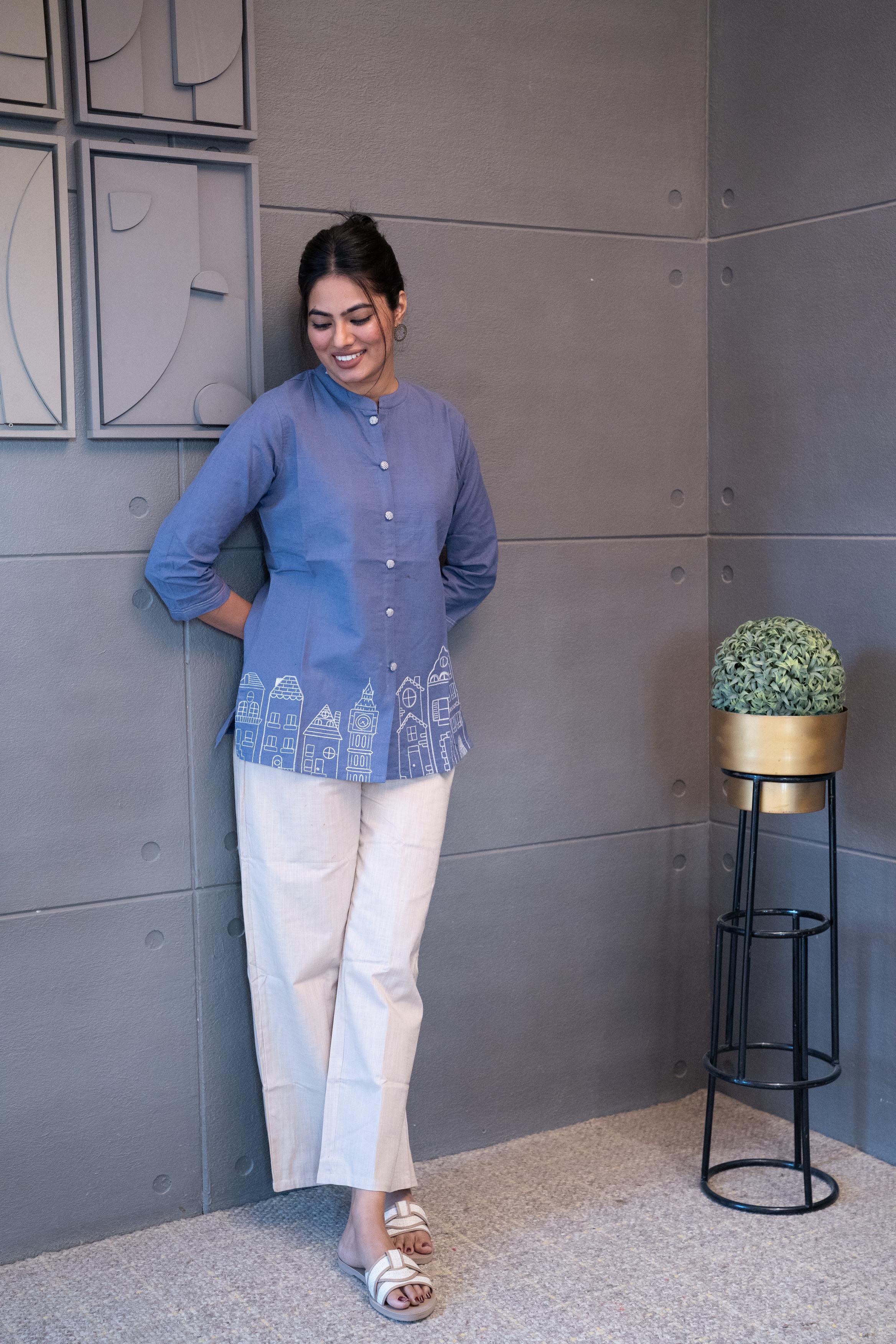 Tanauri Blue Cityscape Short Kurti/Top, folded in clear packaging, showcasing a plain periwinkle blue cotton tunic with subtle button details on the front placket
