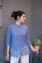 Model wearing Tanauri Blue Cityscape Short Kurti/Top, displaying the periwinkle blue cotton short kurti paired with white pants for a fresh and casual everyday look