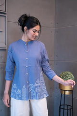 Tanauri Blue Cityscape Short Kurti/Top, folded in clear packaging, showcasing a plain periwinkle blue cotton tunic with subtle button details on the front placket