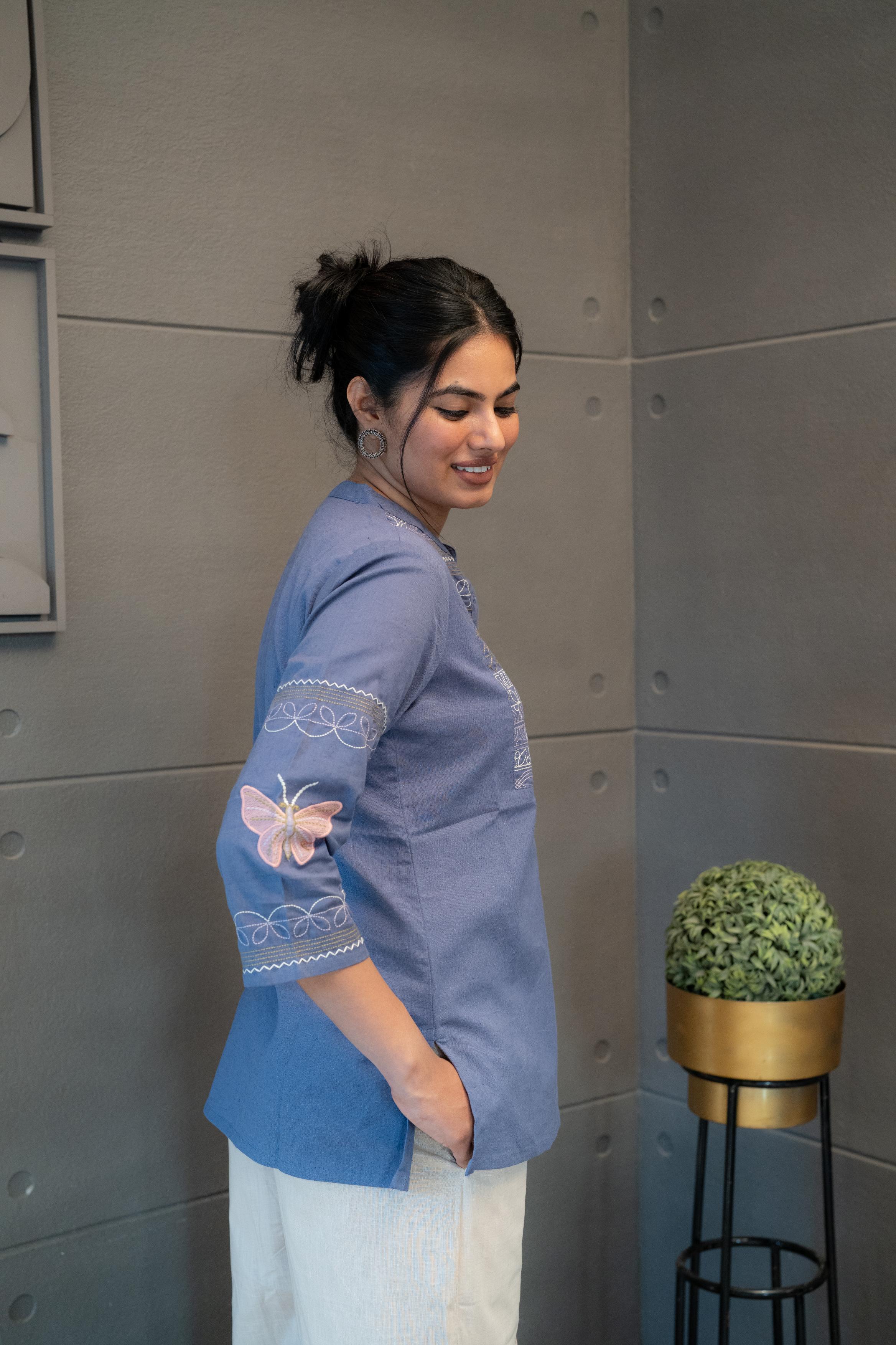 Tanauri Orchid Short Kurti/Top, folded in clear packaging, showcasing a blue cotton tunic with intricate white multi-patterned embroidery on the front and a band collar