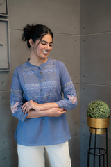 Model wearing Tanauri Orchid Short Kurti/Top, displaying the blue cotton short kurti/top with detailed embroidery and band collar, paired with white pants for an elegant ethnic-casual look