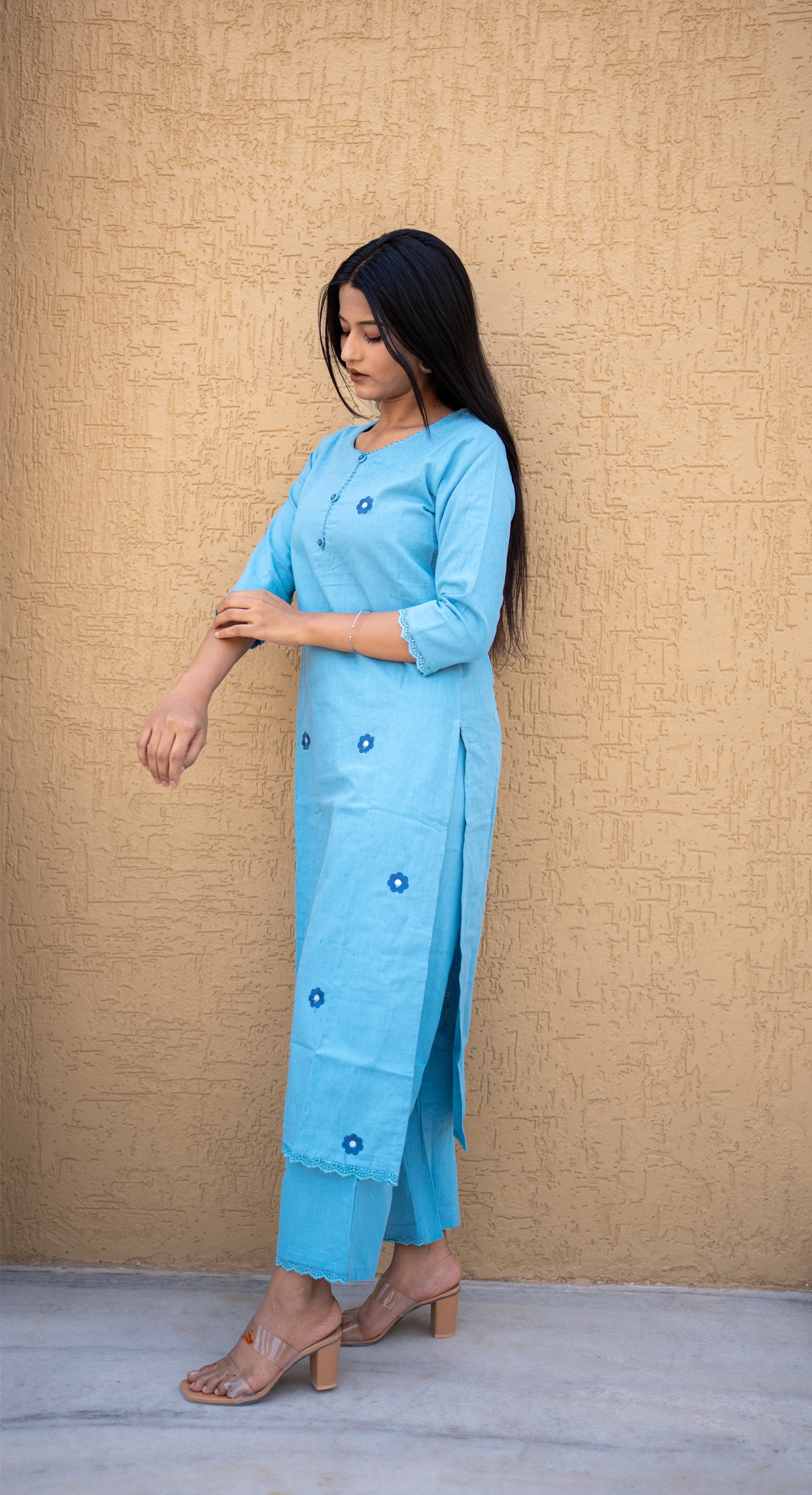 Woman wearing a light blue kurta with pants against a beige wall.