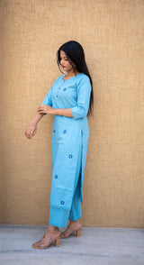 Woman wearing a light blue kurta with pants against a beige wall.