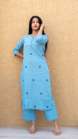Woman wearing a blue kurta with buttons against a beige wall.