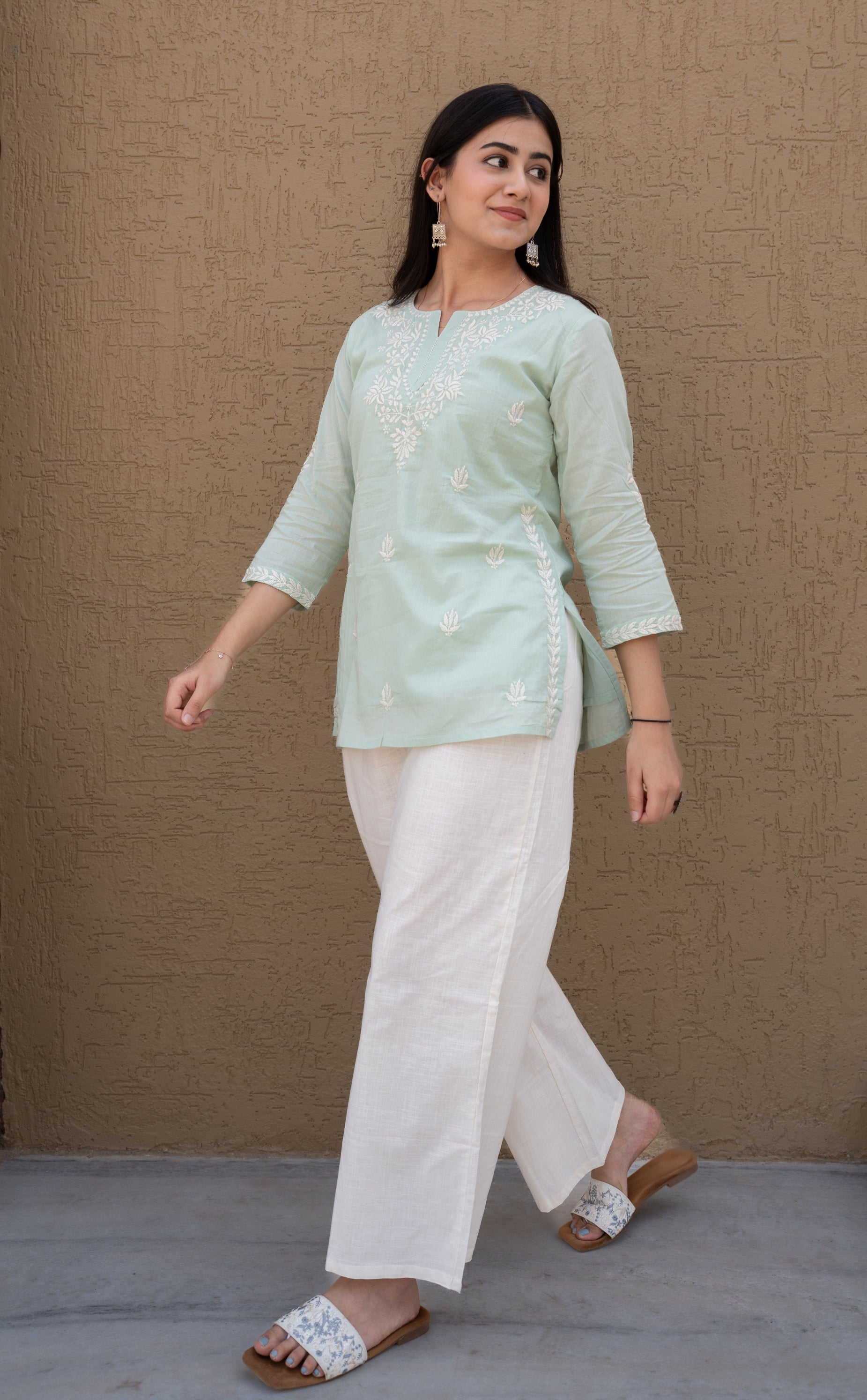 Woman wearing a light green top and white pants against a beige background