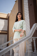 Woman in light green top and beige pants standing on a staircase with buildings in the background