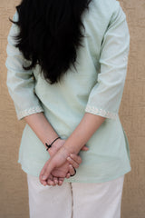 Person wearing a light green top with lace trim on sleeves against a beige background